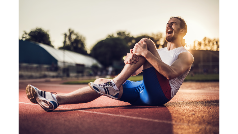 Injured male athlete screaming in pain at sunset.