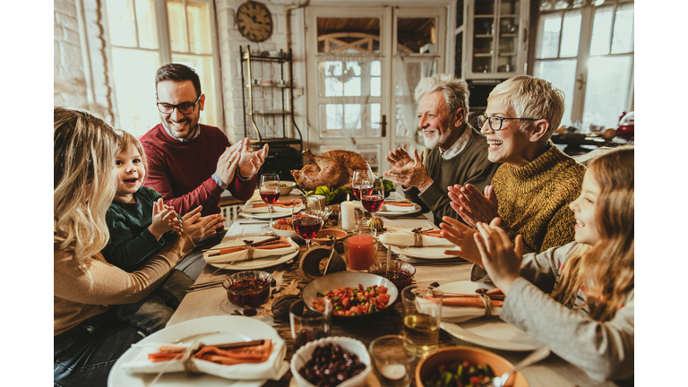 Happy extended family applauding during Thanksgiving meal at dining table.