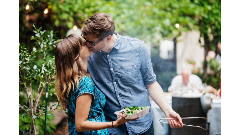 Couple Kissing While Cooking At Family BBQ