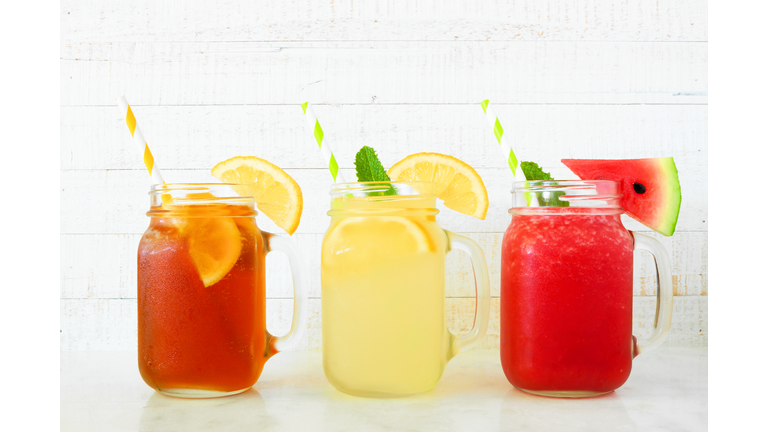 Iced tea, lemonade and watermelon juice summer drinks in mason jar glasses against white wood