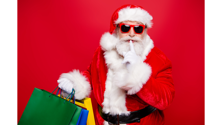 Winter noel eve Christmastime black Friday. Excited hearsay news mature aged grandfather Santa in gloves spectacles white beard package hold forefinger near lips quiet sign isolated red background