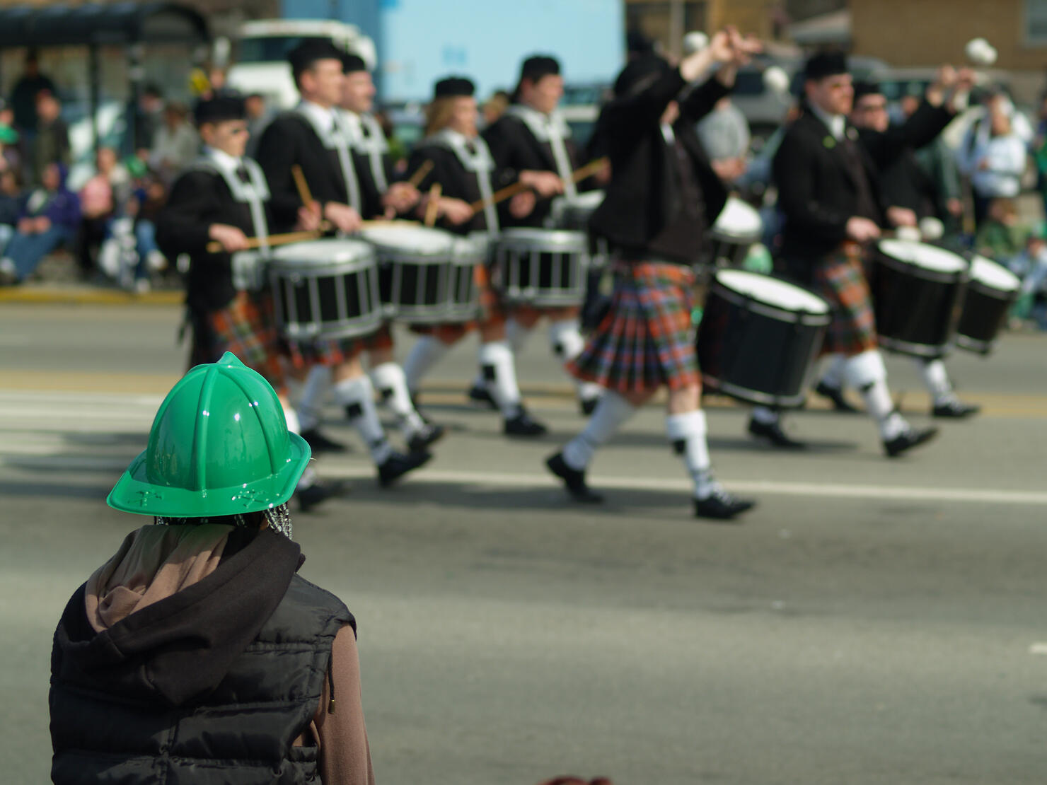 Person in green hat watching drummers walk by in the parade