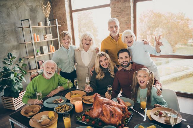 Photo of big family standing hugging feast table holiday roasted turkey making portrait relatives multi-generation raising wine glasses show v-sign in living room indoors