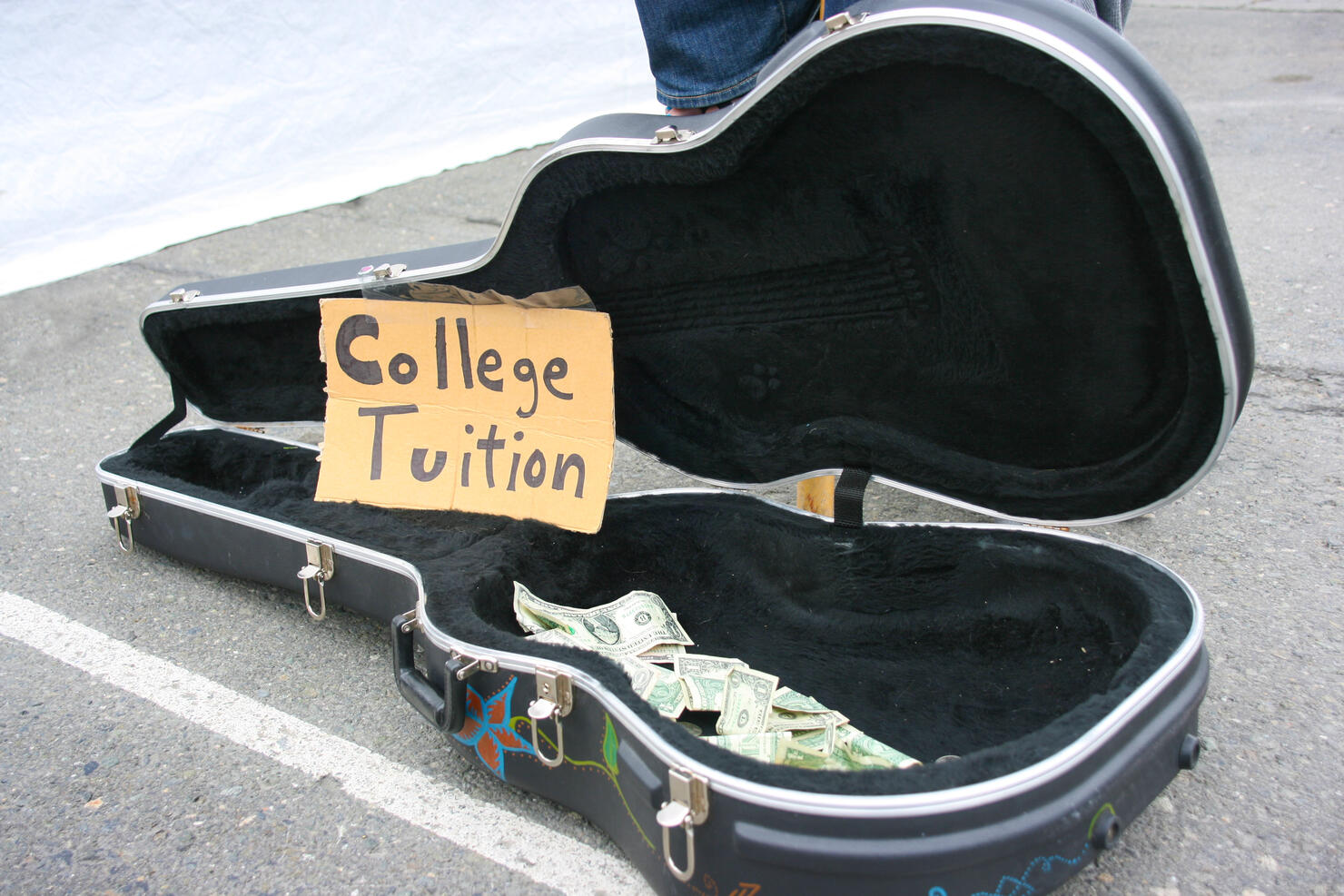 Guitar case open with money for tips with "College Tuition" sign