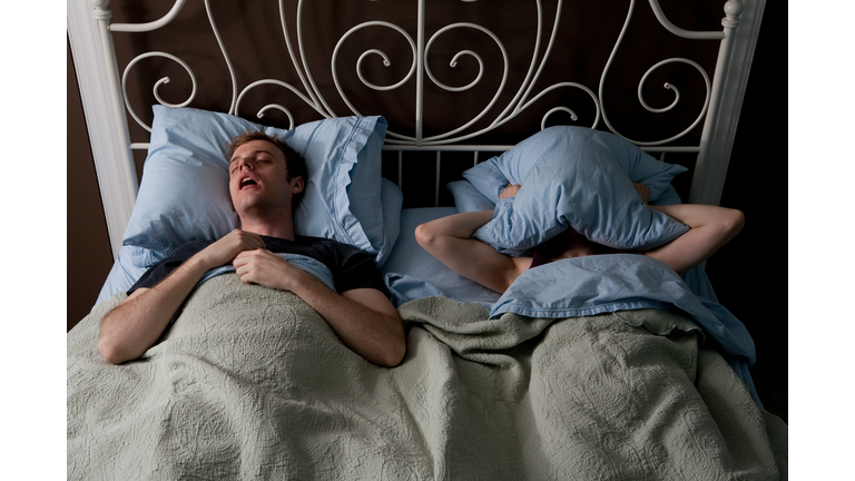 Young man snoring, woman covering face with pillow