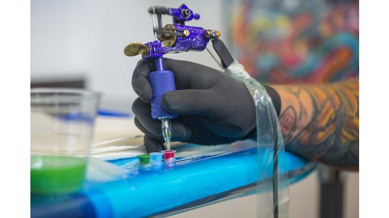 Close up of tattooist hand dipping tattoo gun's needle into red ink