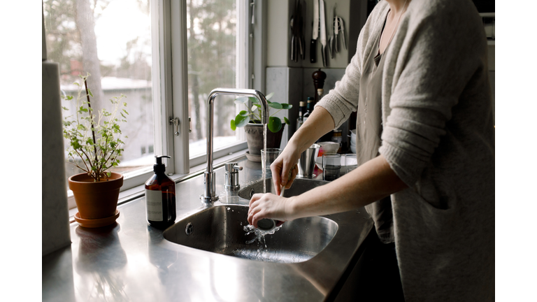 Midsection of woman cleaning cup in kitchen sink at home