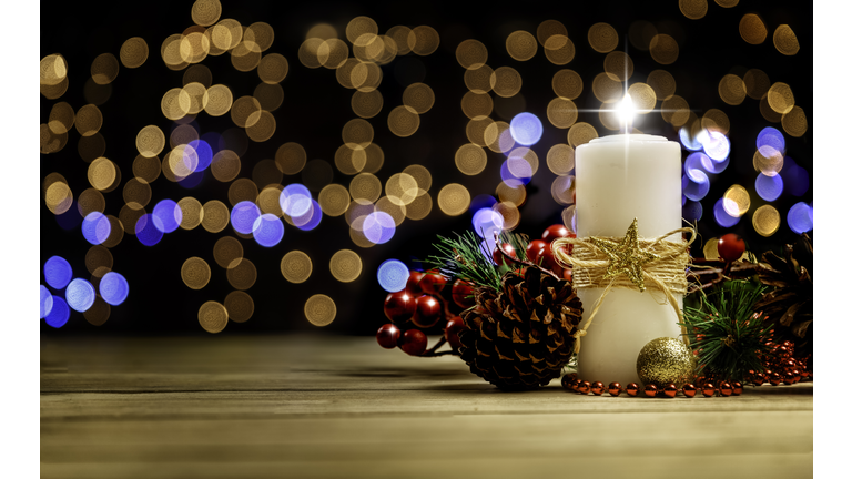 Low key of lit candle on defocused Christmas lighting background