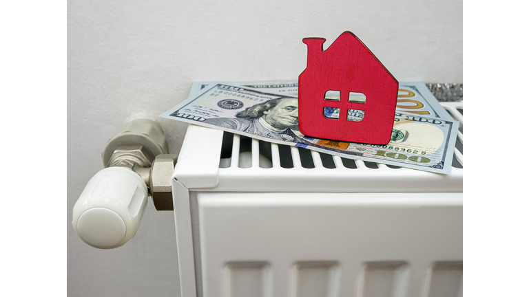 A small red house and cash on the heater at home. Symbolic image of energy efficient,  payment and heating savings in winter.