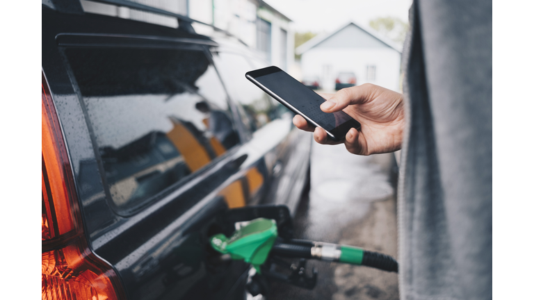 Man using mobile phone while refueling car at gas station