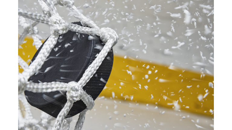 Close-up of an Ice Hockey puck hitting the back of the net as snow flies, side view
