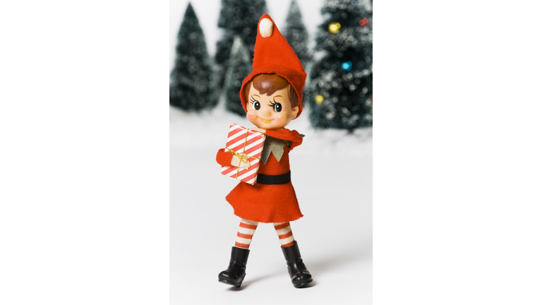 Elf on the shelf holding present standing in snow