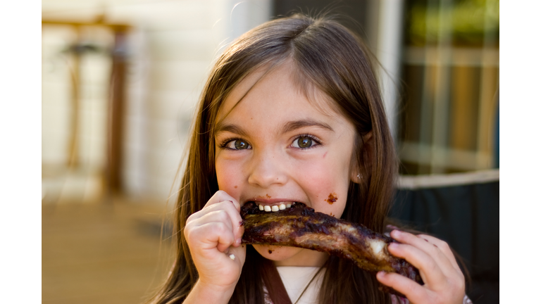 A young girl chowing down on a rib