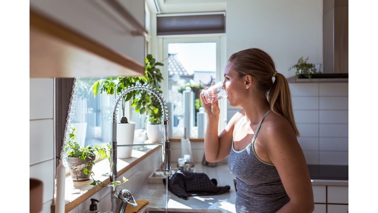 Side view of woman in sports clothing drinking water at kitchen