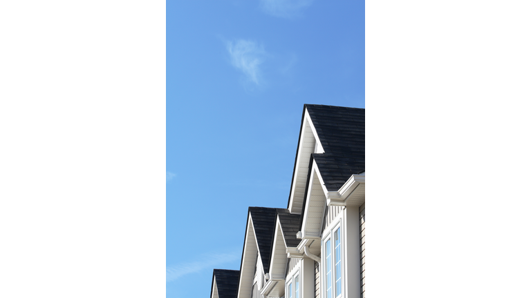 Row of roofs and eaves of homes with blue sky