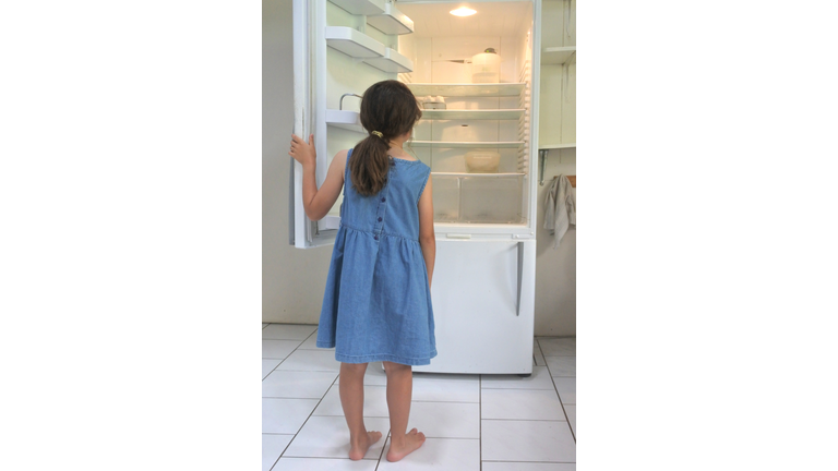 Hungry poor sister girl looks for food in empty fridge at home