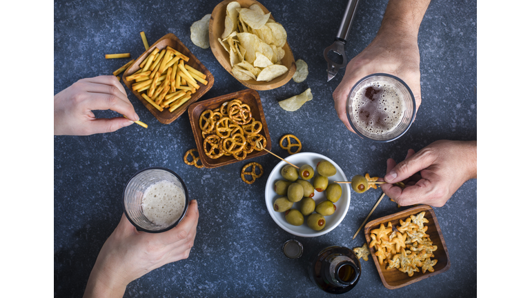 Hands holding glasses with beer on a table. Couple drinking beer and eating snacks