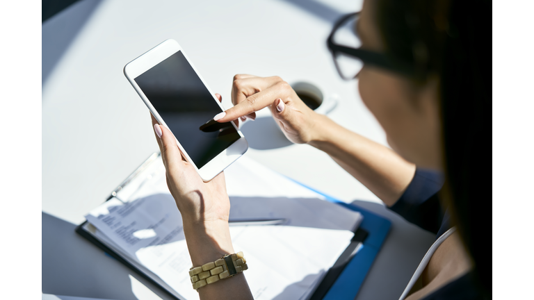 Close-up of businesswoman using cell phone at desk in office