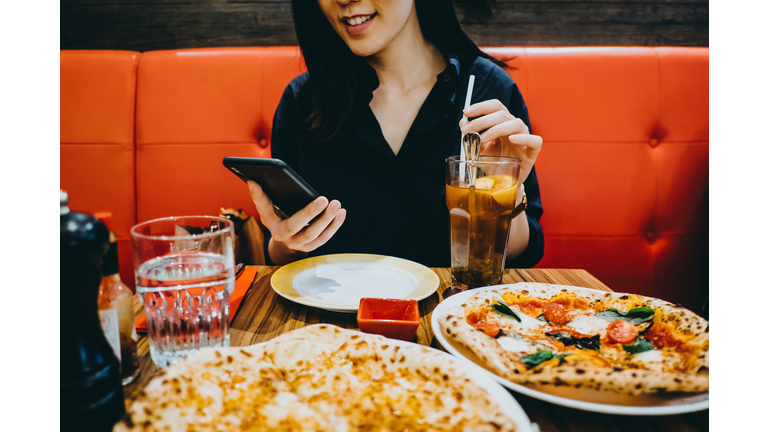 Smiling young woman text messaging on smartphone while dining out in a restaurant