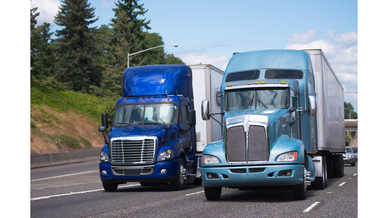 Two big rigs semi trucks in blue tone and different models with trailerd driving side by side