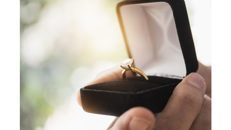 Close up of mans hand holding open box with engagement ring