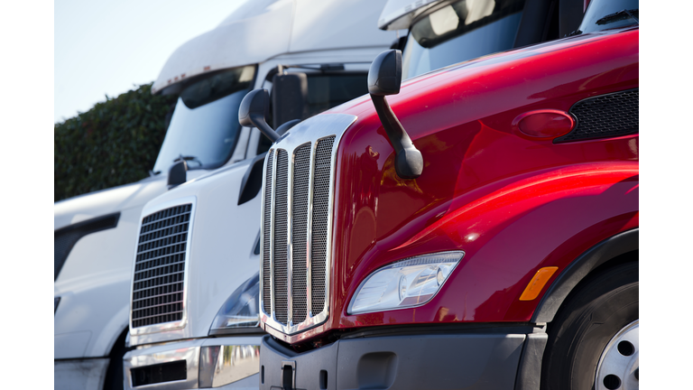 Red and white big rig semi trucks with grilles standing in line on truck stop lot