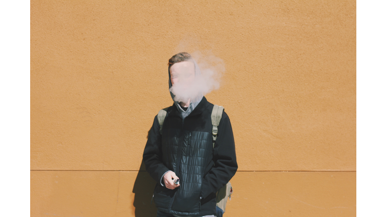 Young Man Smoking While Standing Against Wall On Sunny Day