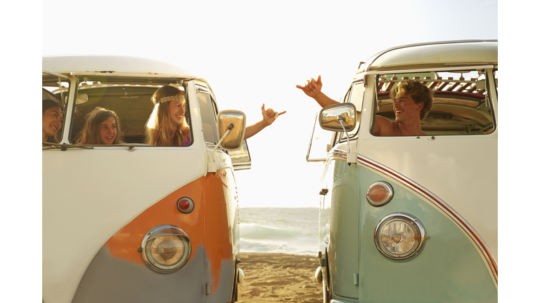 People making hand gestures in vans on beach