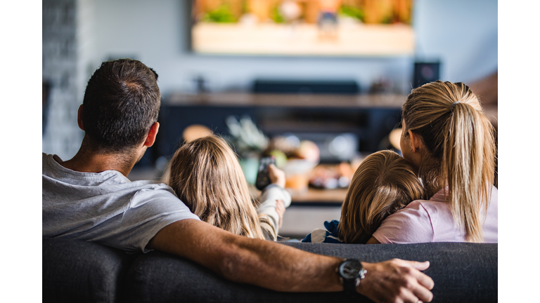 Rear view of a family watching TV on sofa at home.