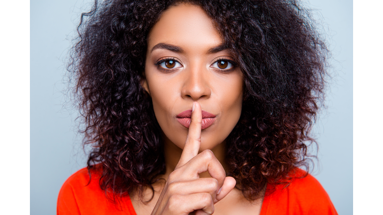 Shh! Closeup portrait of mysterious charming woman with modern hairdo asking for keeping silence holding forefinger on plump lips isolated on grey background