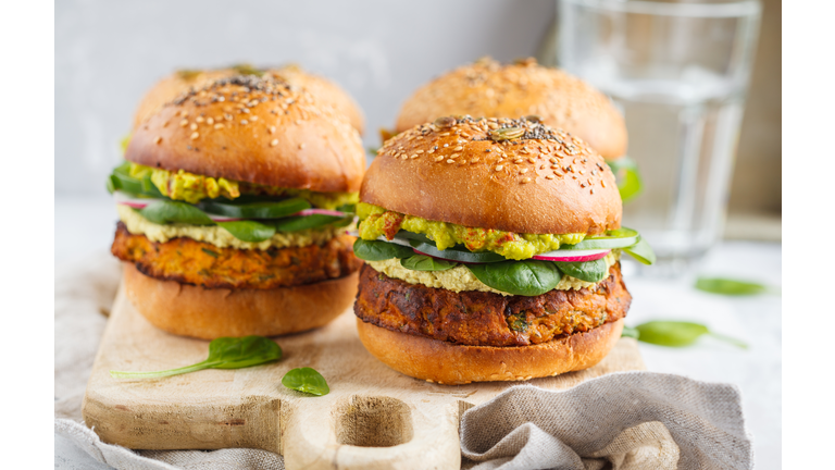 Healthy baked sweet potato burger with whole grain bun, guacamole, vegan mayonnaise and vegetables on a wooden board. Vegetarian food concept, light background.