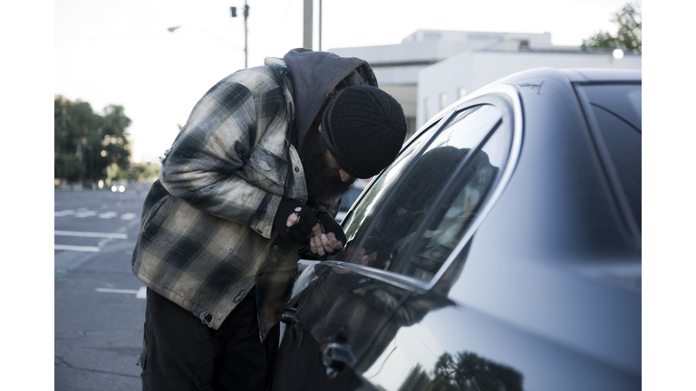 USA, Utah, Salt Lake City, Homeless man breaking into car, side view