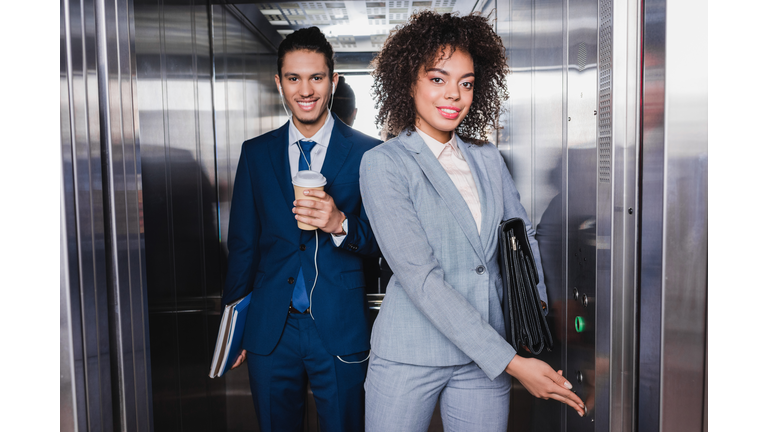 Woman pushing button in elevator by man in earphones with coffee cup