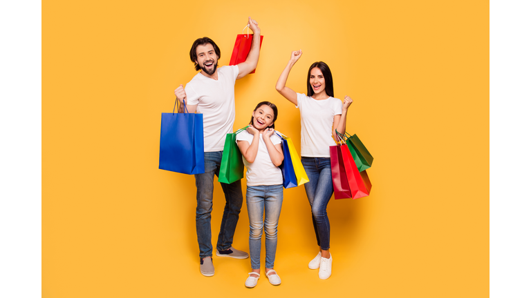 Full length body size view portrait of nice attractive trendy cheerful people holding in hands bags with new clothes having fun rejoice isolated over shine vivid pastel yellow background