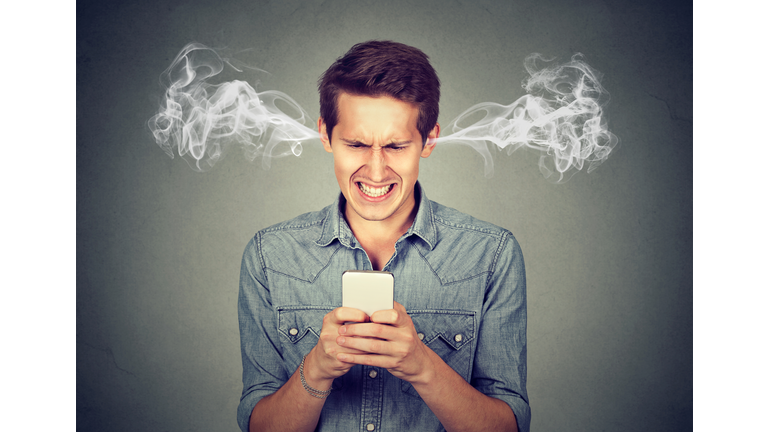 Frustrated angry man reading a text message on his smartphone blowing steam coming out of ears