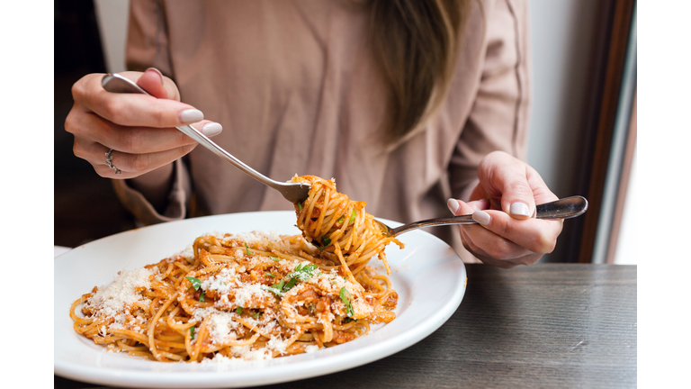 girl eats Italian pasta with tomato, meat. Close-up spaghetti Bolognese wind it around a fork with a spoon. Parmesan cheese