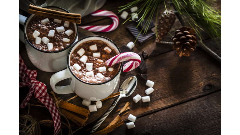 Two homemade hot chocolate mugs with marshmallows on rustic wooden Christmas table