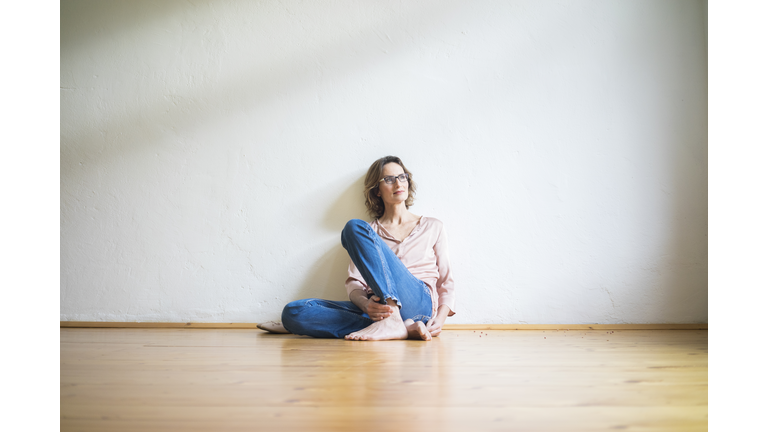 Mature woman sitting on floor in empty room thinking