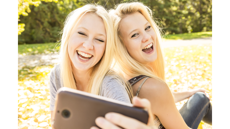 Two sisters having fun outdoors in a city park in autumn and laughing at the selfies they have taken of themselves