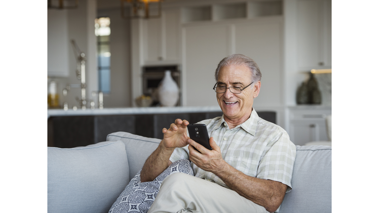 Caucasian man sitting on sofa texting on cell phone