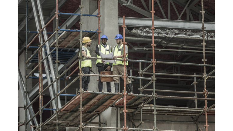 Construction workers and businessman discussing building plan on scaffolding