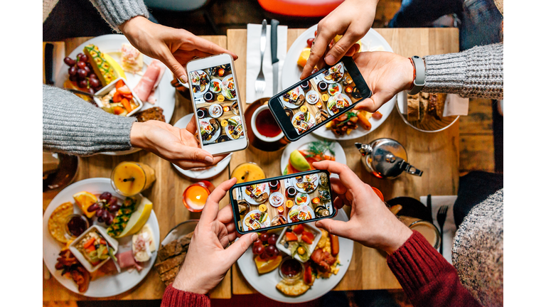 Friends taking pictures of food on the table with smartphones during brunch in restaurant