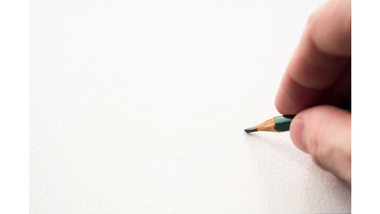 Hand holding pencil touching a blank sheet of paper
