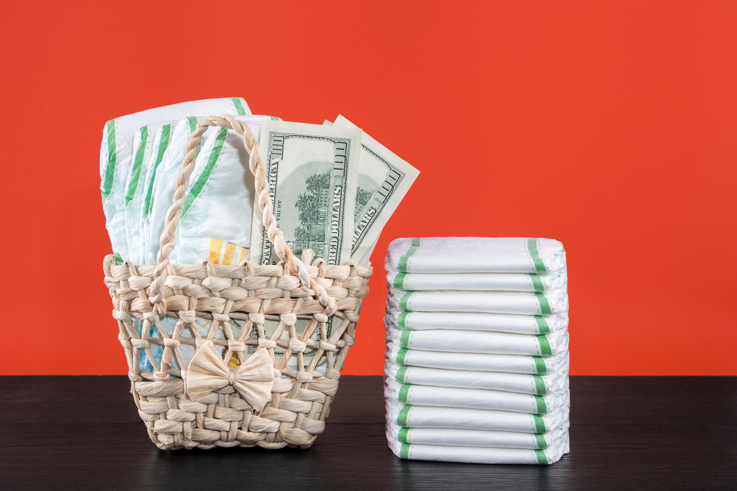 Wicker basket with baby diapers and dollars, stack of diapers, wood