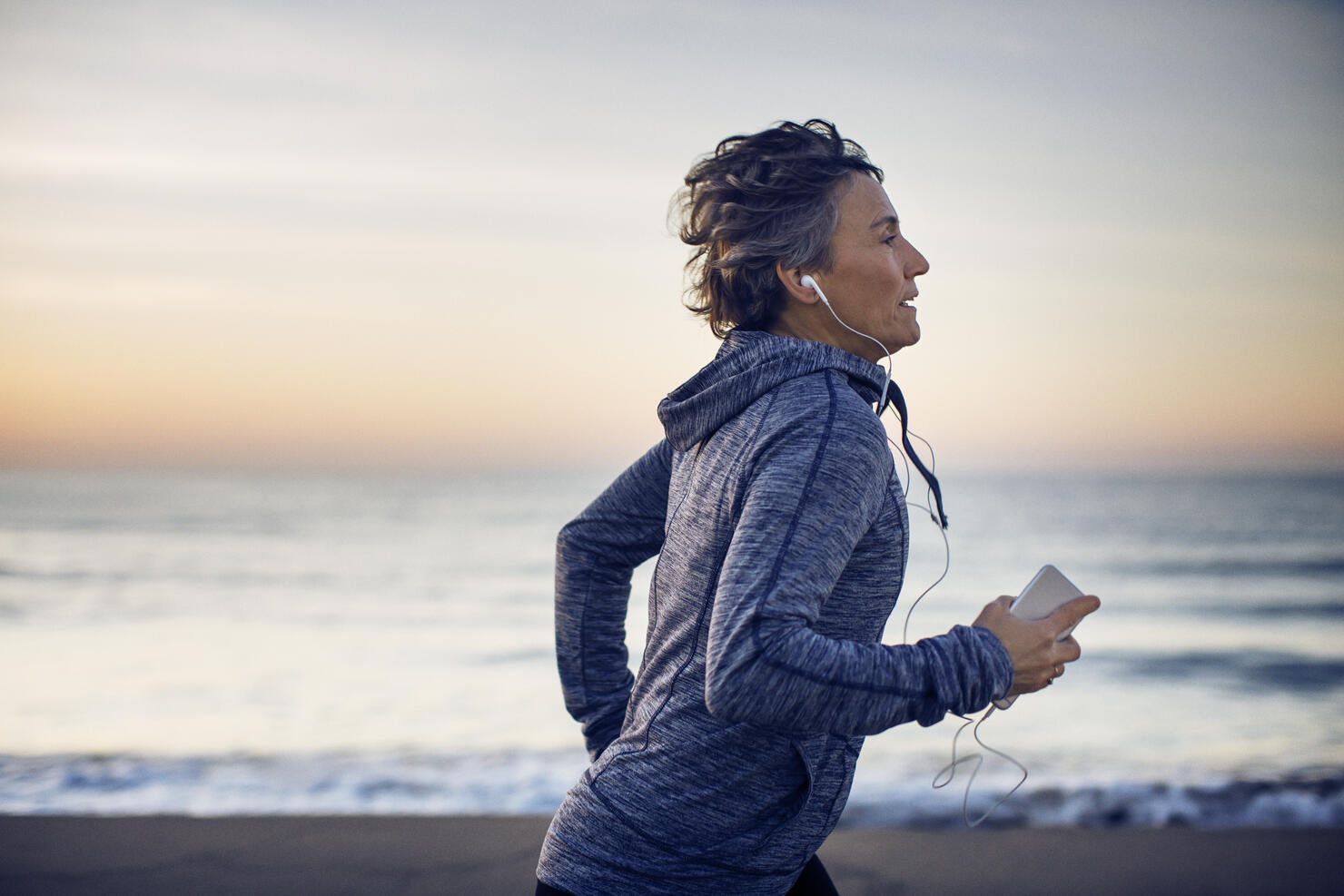 Woman jogging while listening music at beach against sky