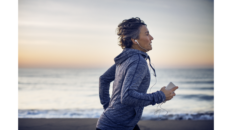 Woman jogging while listening music at beach against sky