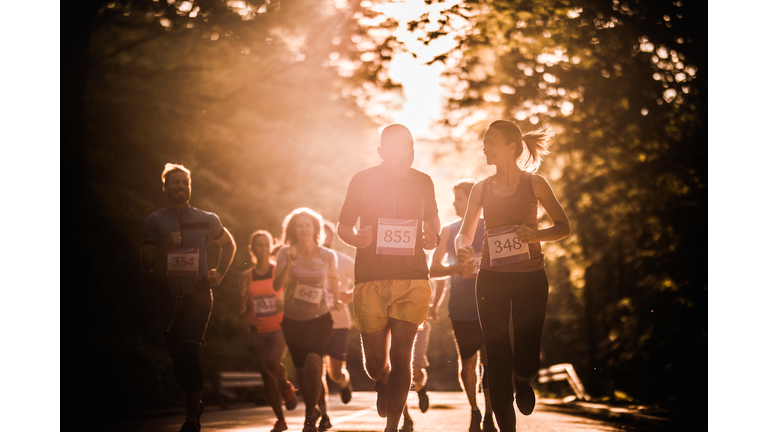 Large group of athletic people running marathon race in nature at sunset.