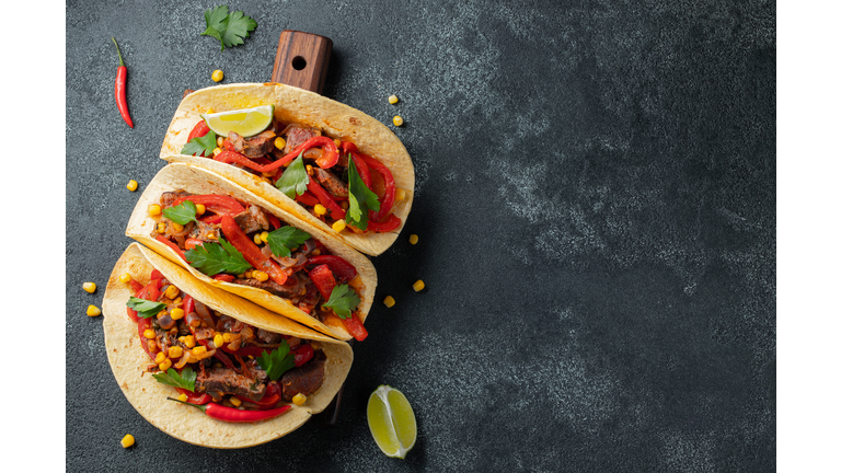 Mexican tacos with beef, vegetables and salsa. Tacos al pastor on wooden board on black background. Top view with copy space