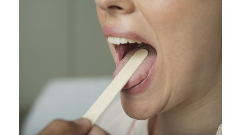 Woman having mouth examined with tongue depressor, cropped