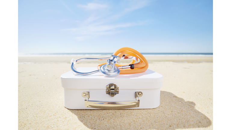 Stethoscope and suitcase on beach by the sea, symbol for travel pharmacy/ first aid kit